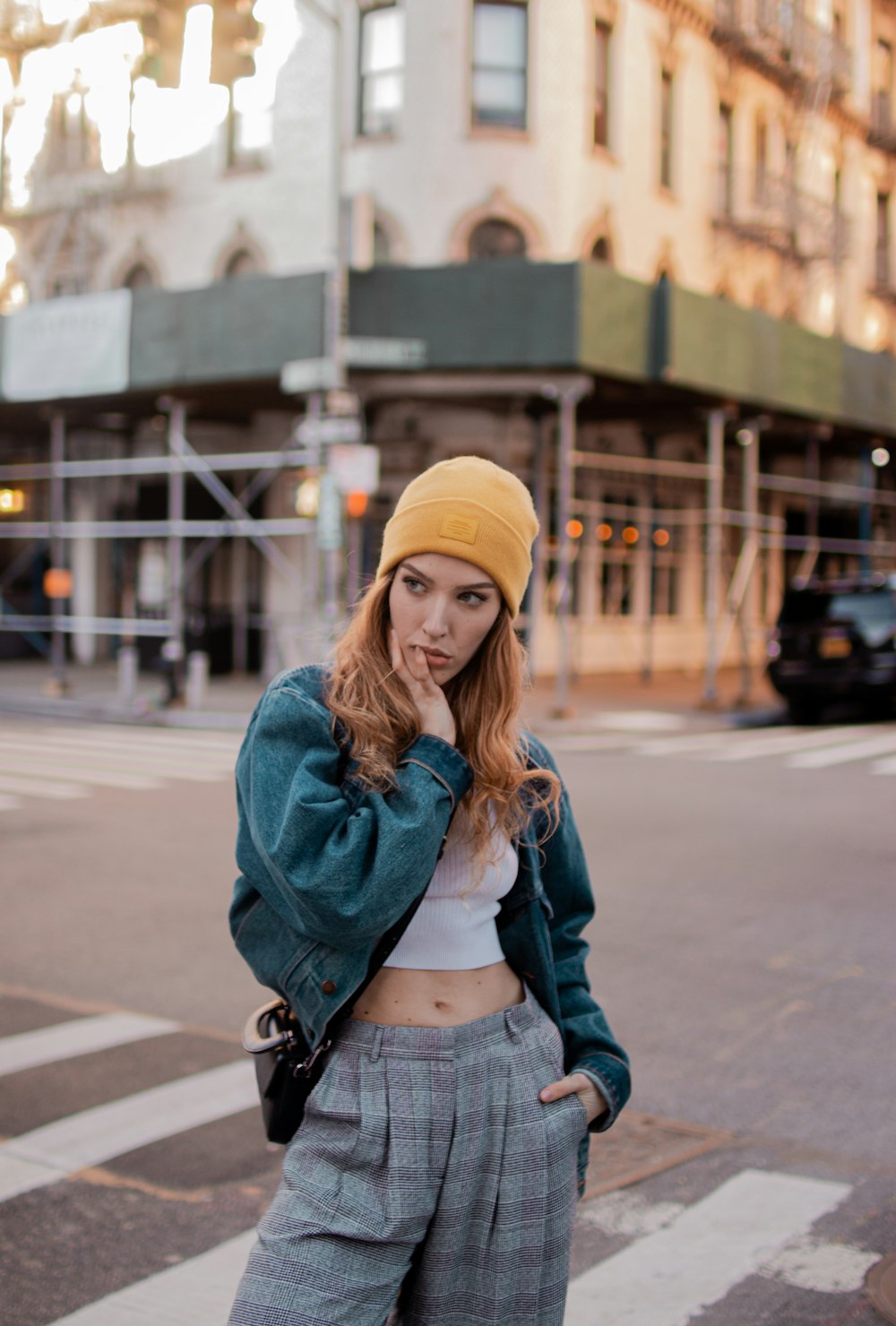 woman in blue denim jacket and yellow knit cap standing on sidewalk during daytime