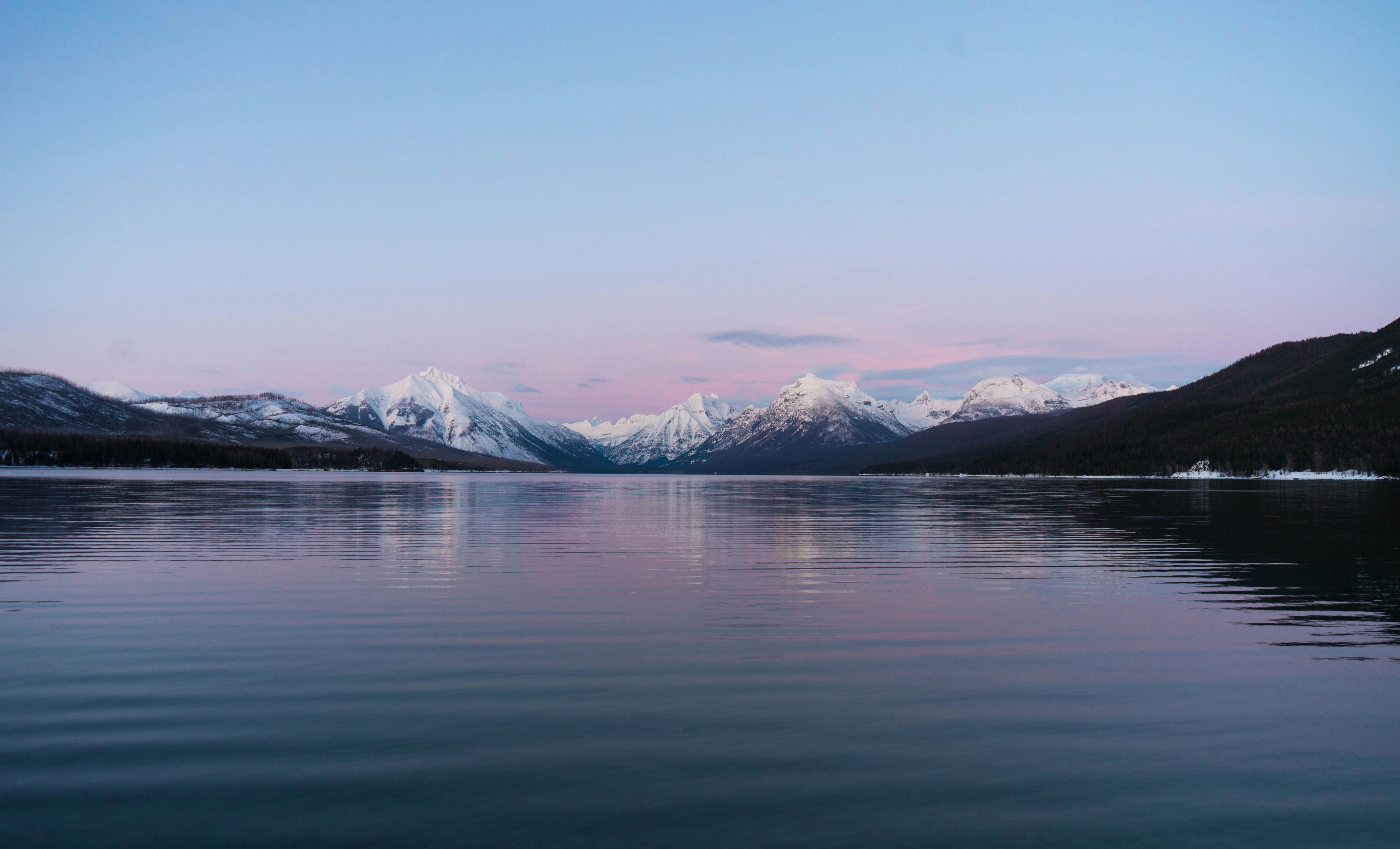 snow covered mountains near lake during daytime, a breathtaking view of blue hour at Lake McDonald, MT.