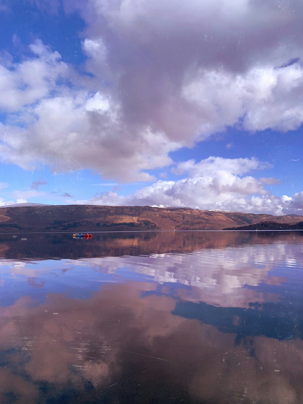 brown mountain near body of water under blue sky and white clouds during daytime