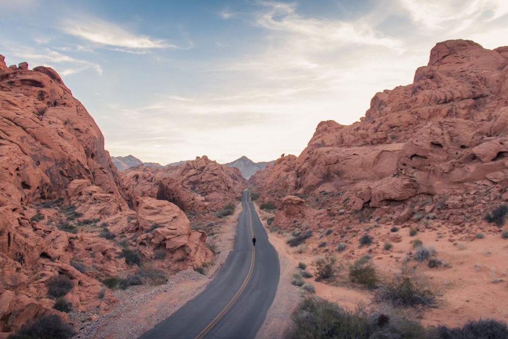 gray asphalt road between brown rock formation under white clouds during daytime