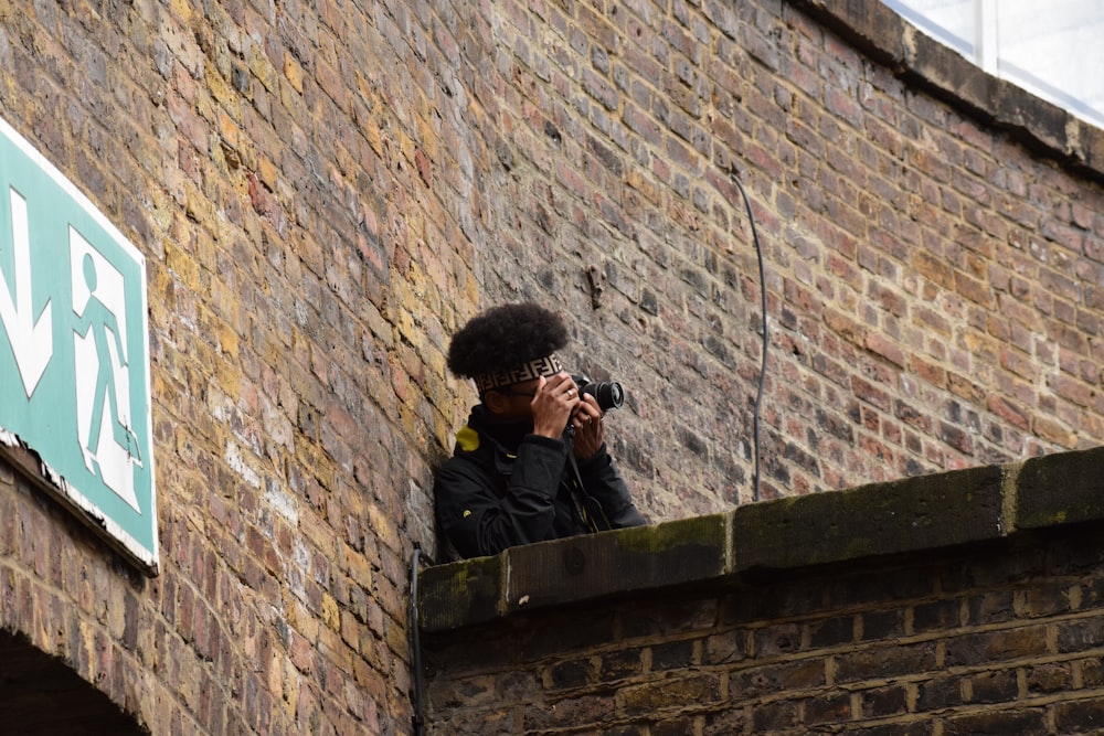 茶色のレンガの壁の写真を撮る黒いジャケットの男