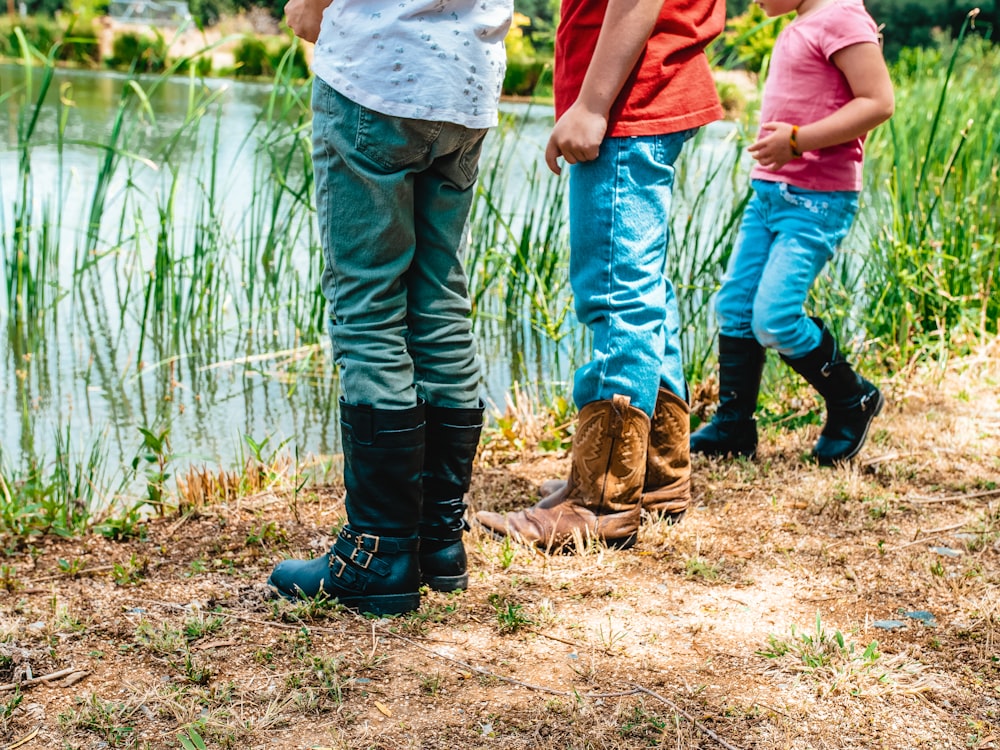 man in blue denim jeans and brown leather boots standing beside body of water during daytime