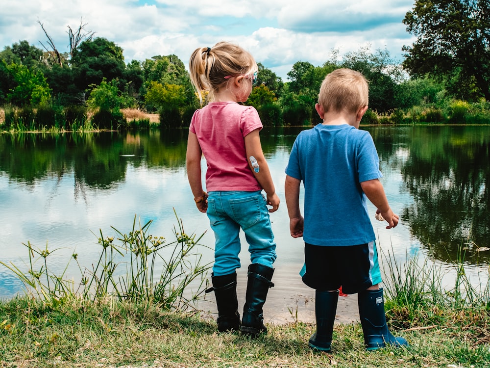 2 Jungen, die tagsüber auf grünem Gras in der Nähe des Sees stehen