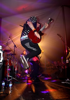 man in black and white long sleeve shirt playing guitar on stage