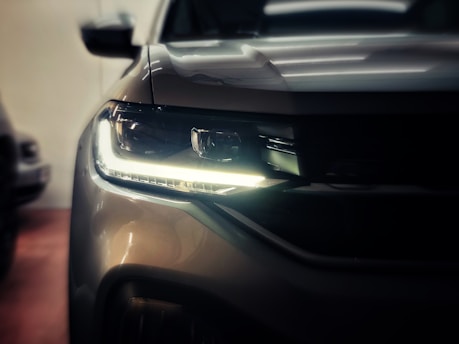 A close-up view of a car headlight, showcasing a modern and sleek design with illuminated LED elements. The image focuses on the front right section of the vehicle, capturing the curves and metallic finish of the car's exterior.