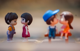 Two pairs of small figurines depicting young couples facing each other. The background is softly blurred to enhance the focus on the figurines. One pair stands facing each other, while the other pair is sitting, creating a warm, playful atmosphere.