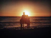 A joyful family posing in front of a tropical beach at sunset, capturing a memorable vacation moment.