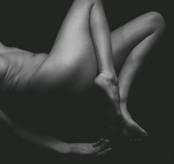 A monochromatic photograph showcasing a partially visible human body in a relaxed pose against a dark background, emphasizing the curves and lines of the skin.