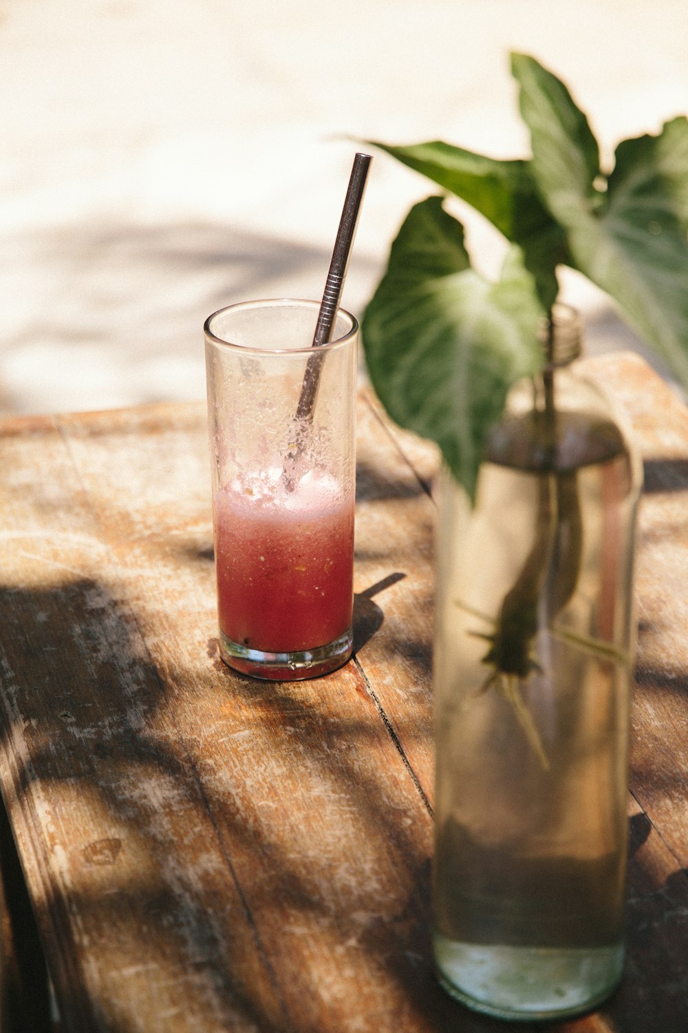 clear drinking glass with red liquid and black straw on brown wooden table