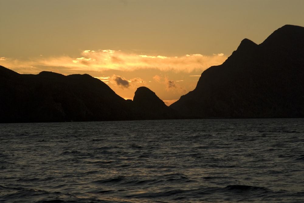 silhouette of mountains and body of water during sunset