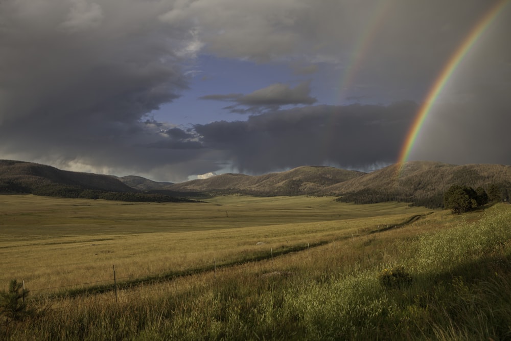 green grass field near mountains under white clouds and blue sky during daytime