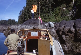 man in brown jacket and brown pants standing beside brown wooden boat on rocky hill during