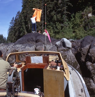 man in brown jacket and brown pants standing beside brown wooden boat on rocky hill during