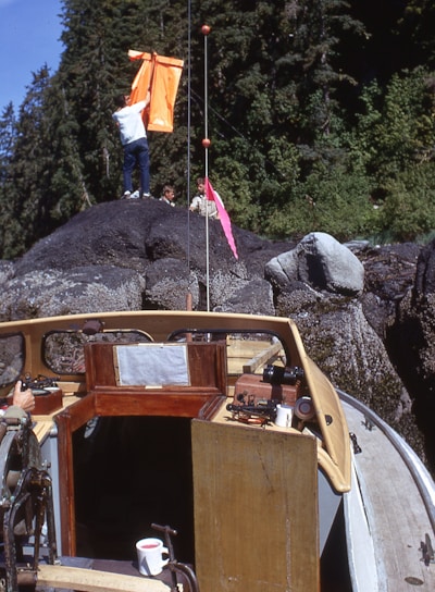 man in brown jacket and brown pants standing beside brown wooden boat on rocky hill during