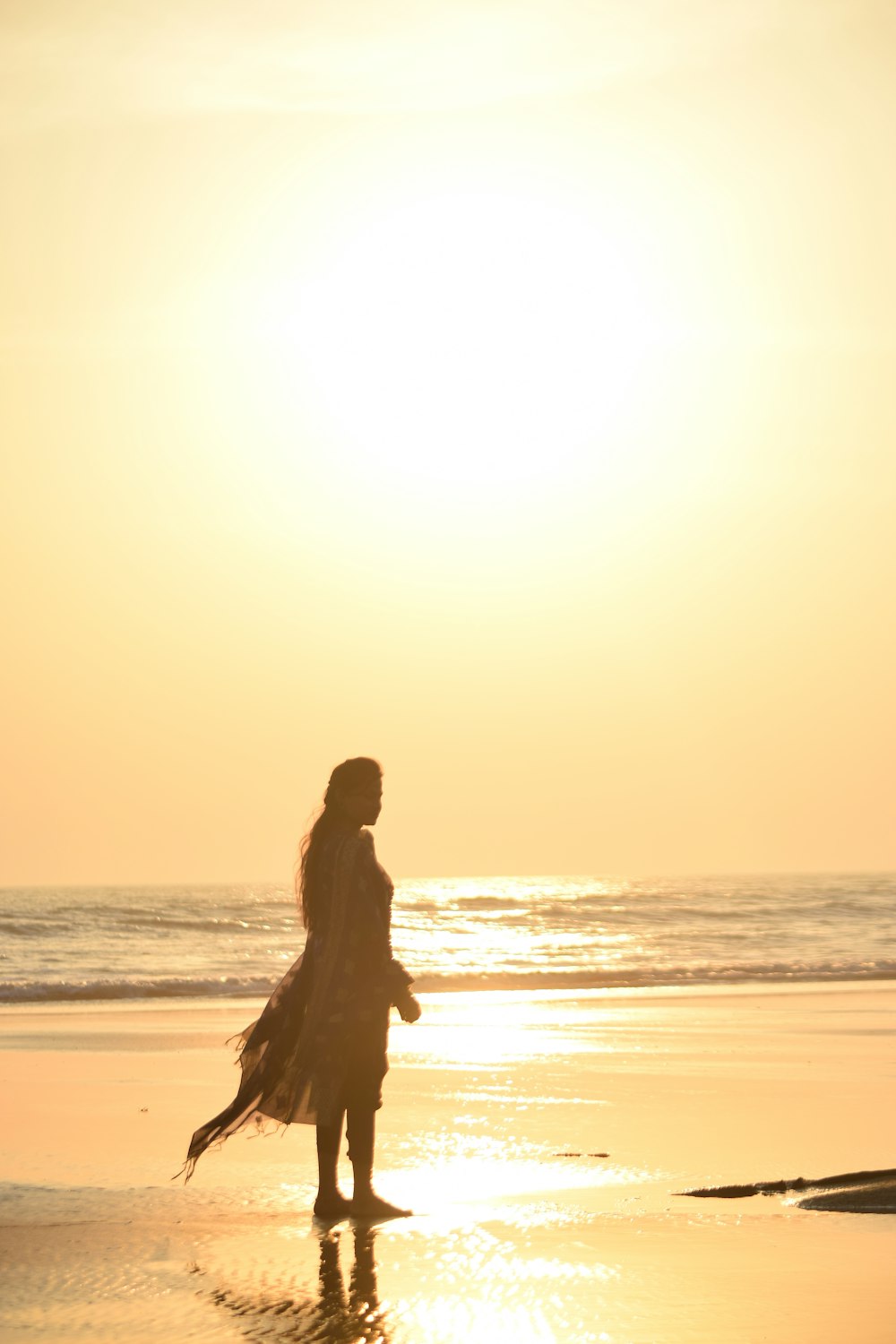 Mujer en vestido negro de pie en la playa durante la puesta del sol