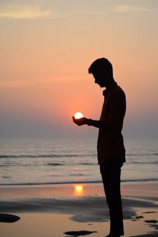 silhouette of man standing on seashore during sunset