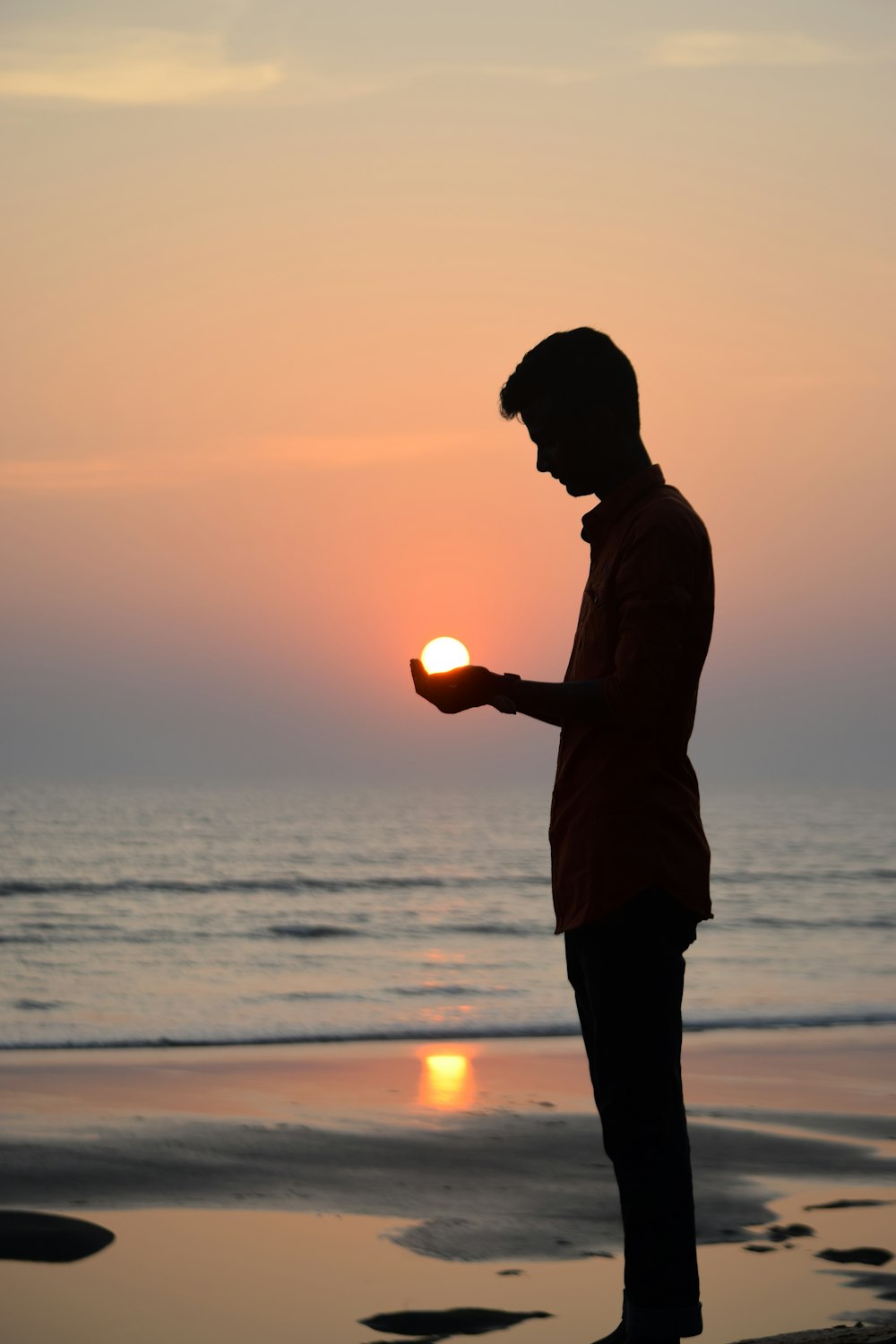 Silueta del hombre de pie en la orilla del mar durante la puesta del sol