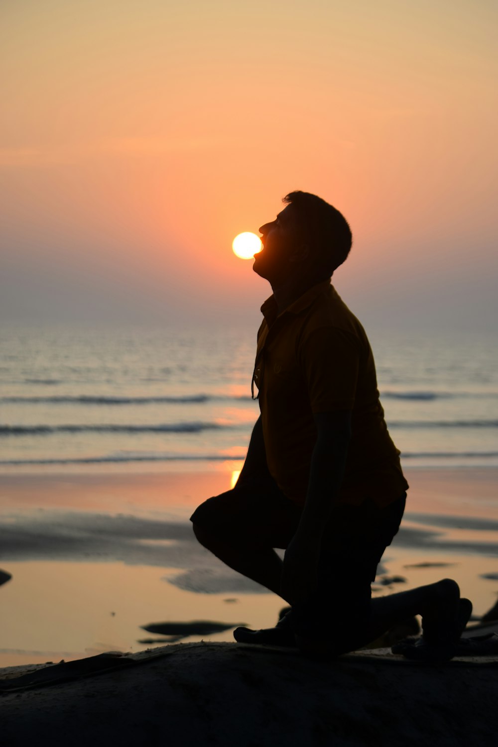 silhouette of man sitting on beach during sunset