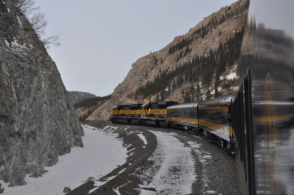 yellow and black train on rail tracks near brown rocky mountain during daytime