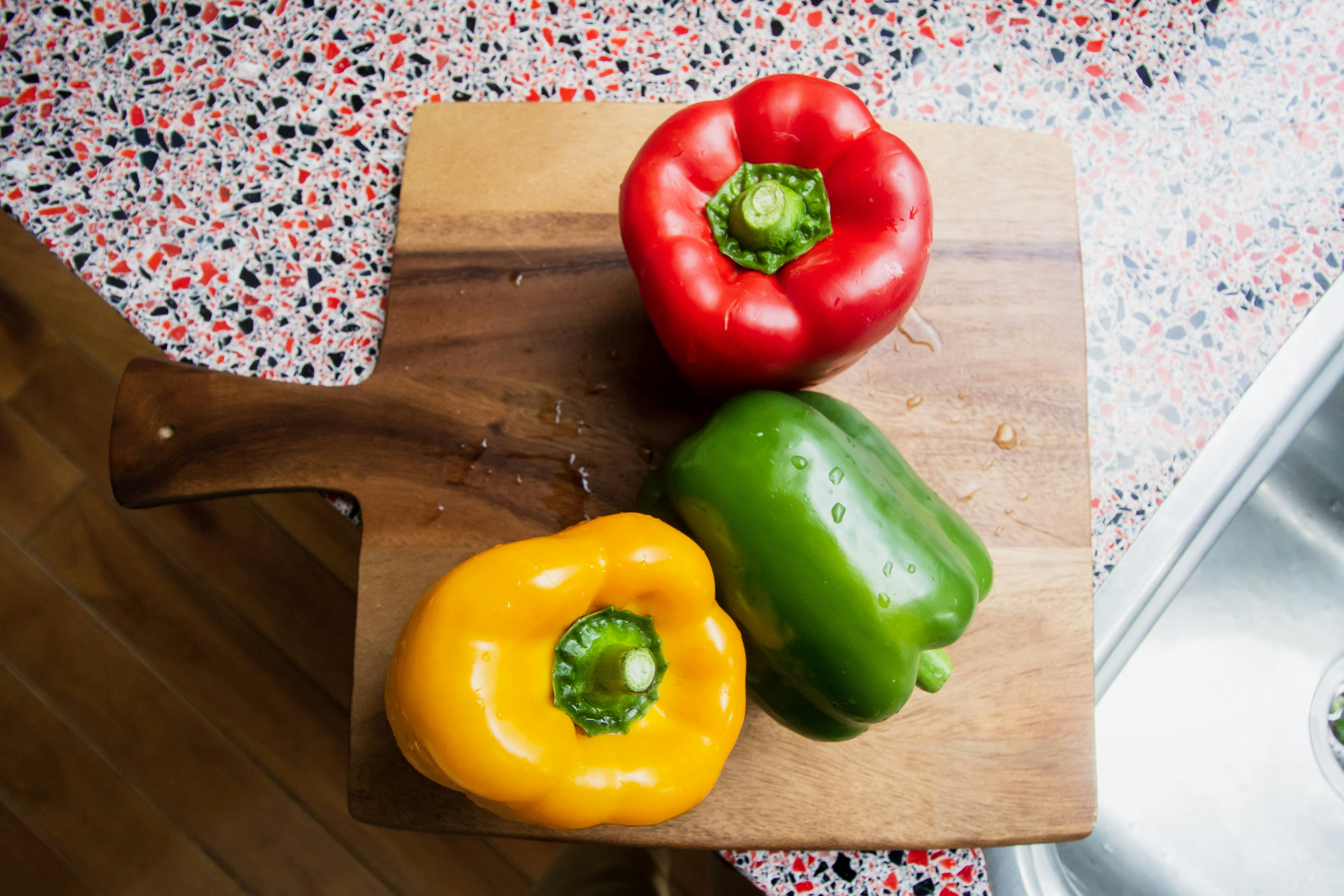 green and red bell pepper on brown wooden chopping board