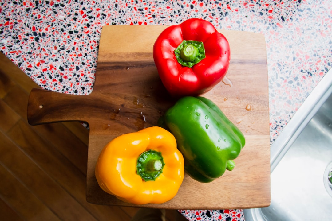 green and red bell pepper on brown wooden chopping board
