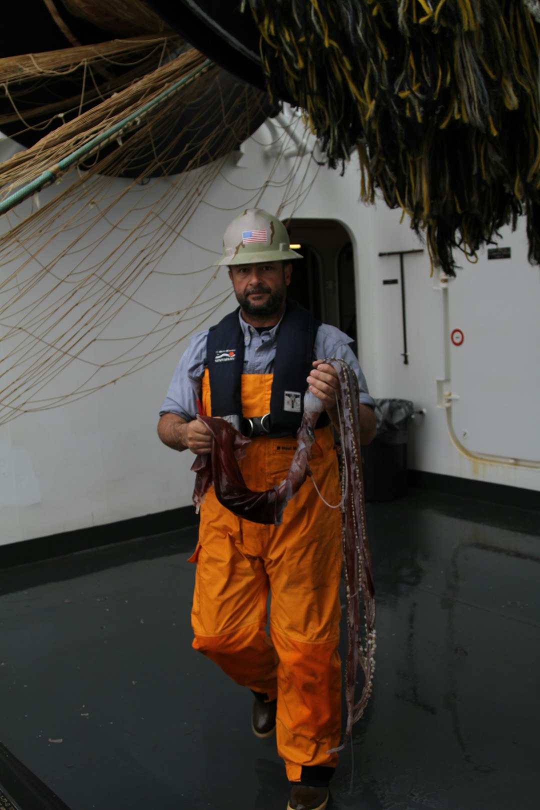 man in blue and orange zip up jacket wearing white helmet standing on boat during daytime