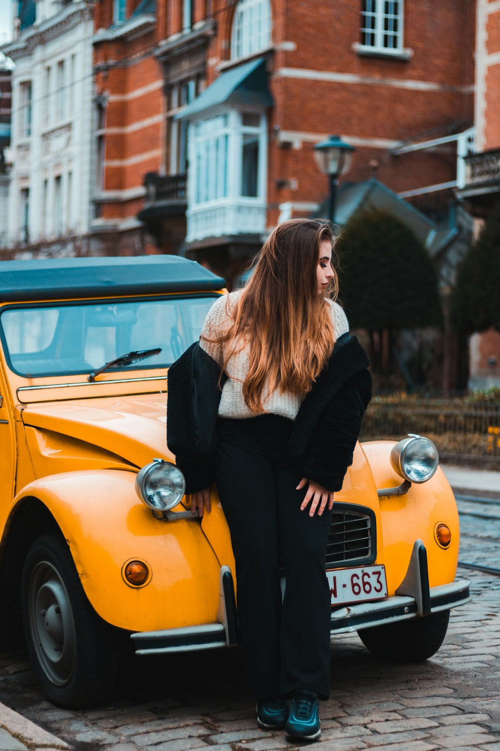 woman in black long sleeve shirt leaning on yellow car