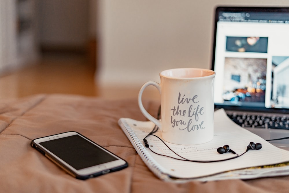 white ceramic mug beside silver iphone 6 on brown wooden table