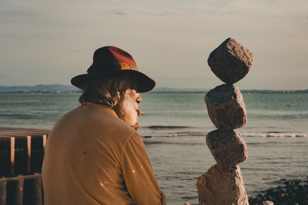 man in brown long sleeve shirt sitting on gray rock near body of water during daytime