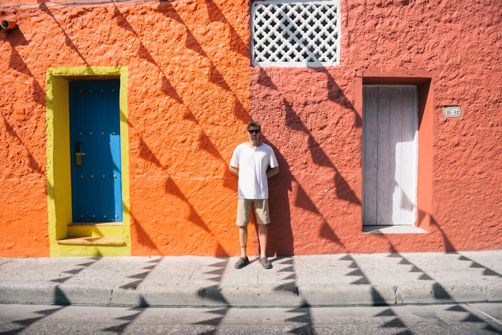 man in white t-shirt and blue shorts standing in front of orange brick wall during