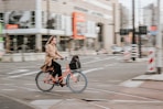 woman in brown coat riding on black bicycle on road during daytime