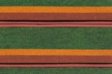Rows of roof tiles are arranged in a detailed, repetitive pattern featuring alternating colors of green, orange, and brown. The tiles have a scale-like texture, creating a visually striking and textured appearance.