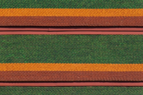 Rows of roof tiles are arranged in a detailed, repetitive pattern featuring alternating colors of green, orange, and brown. The tiles have a scale-like texture, creating a visually striking and textured appearance.