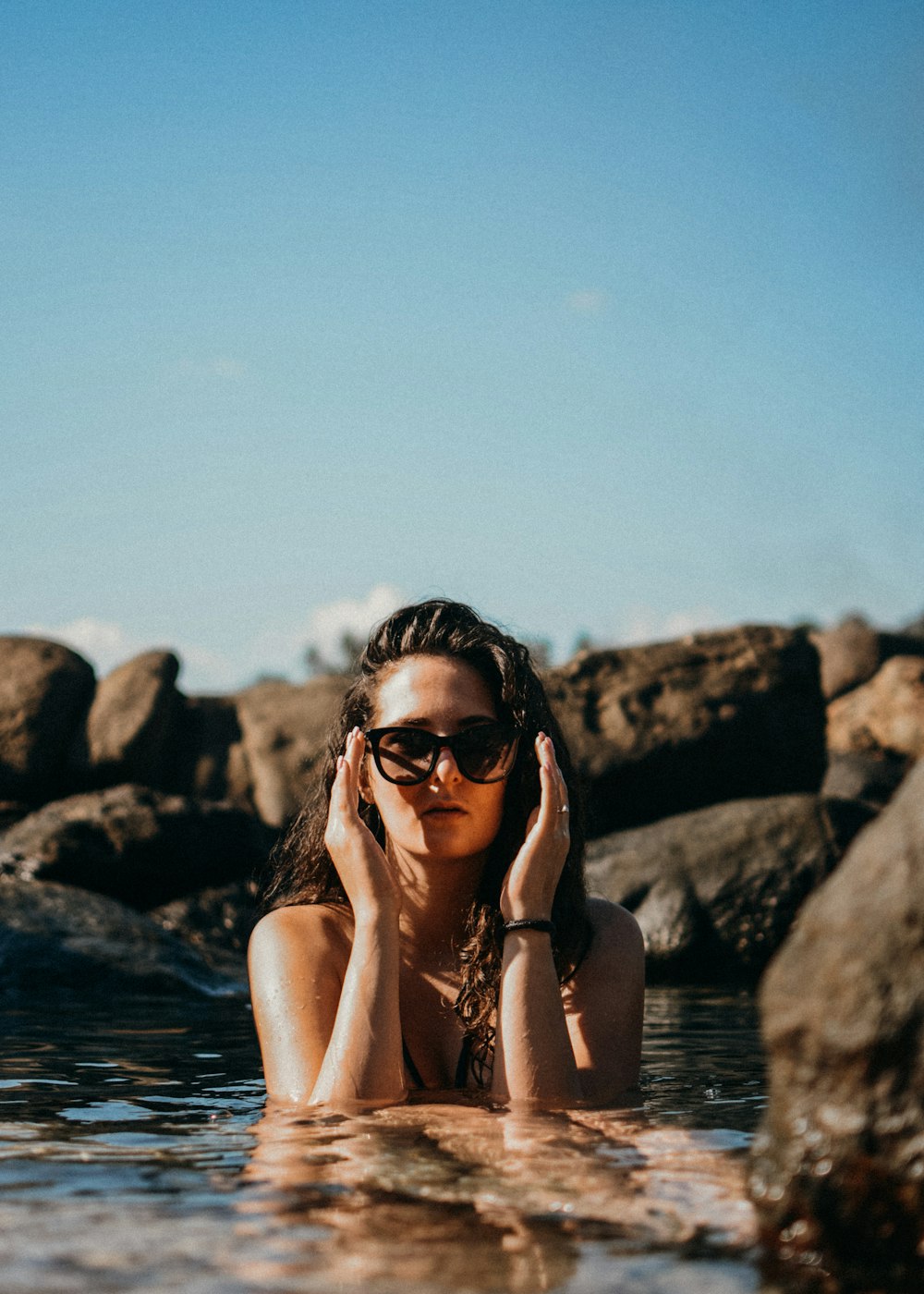 검은 선글라스를 낀 여자가 낮에 수역 근처의 바위에 앉아 있습니다.