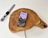 A smartphone displaying a landscape image and battery charging status rests on a wooden charging pad. Nearby, a smartwatch with a red, white, and black striped band lies on a white surface. A charging cable is visible connecting to the wooden pad.