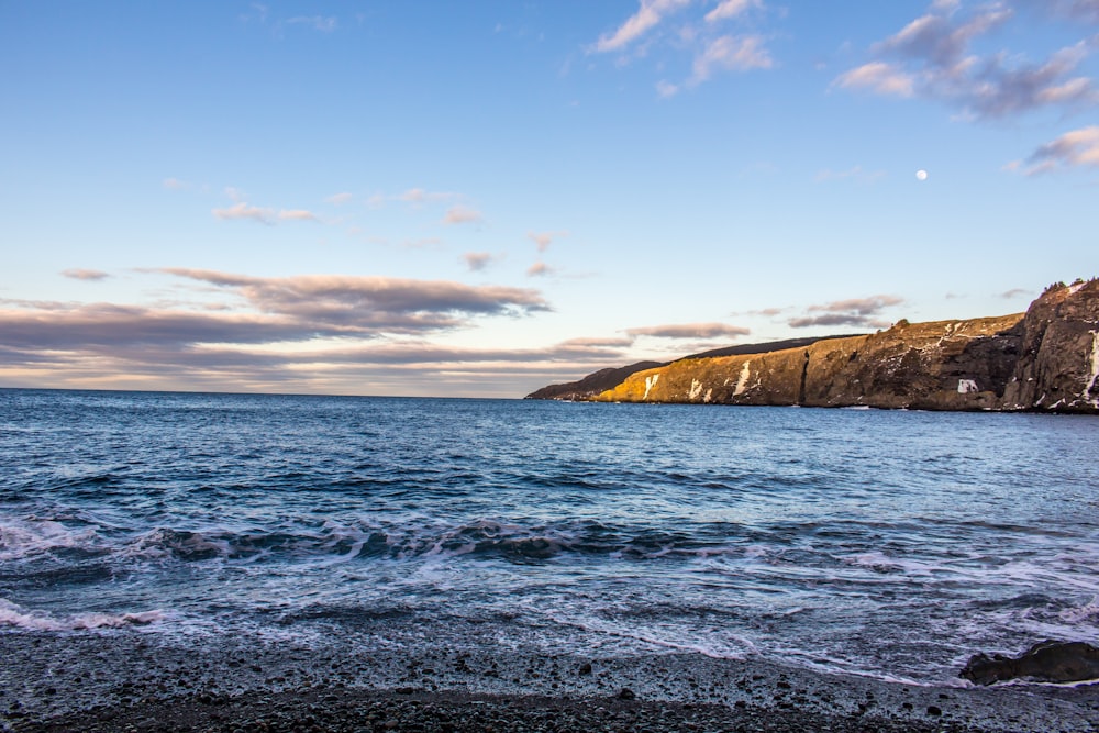 brown rock formation beside body of water under blue sky during daytime