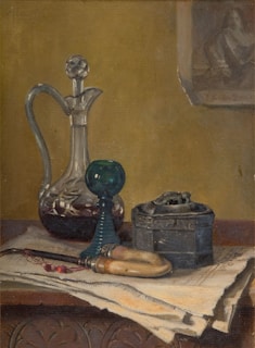A still life painting depicting a table with a crystal decanter, a green glass mouthpiece, a metal box, and a tool with a wooden handle. The objects rest on a pile of papers atop a carved wooden surface. The background is a muted yellow-brown, with a partially visible frame of a painting or photograph.