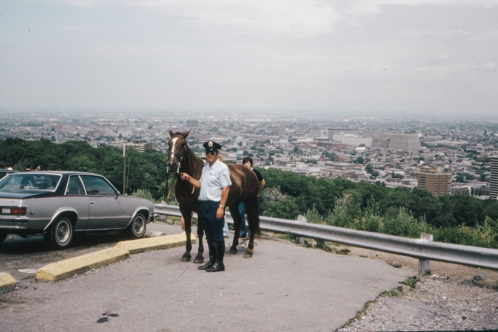 man in white t-shirt and blue denim jeans riding brown horse on road during daytime