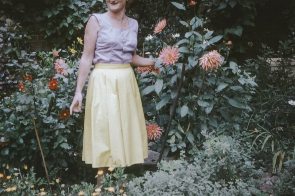 girl in yellow sleeveless dress standing beside red flowers