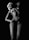 A woman with light hair poses in a floral bikini against a dark background. The image is in black and white, highlighting the contrast between the skin and shadows. Her posture is relaxed yet confident, with one arm raised above her head and the other resting on her waist.