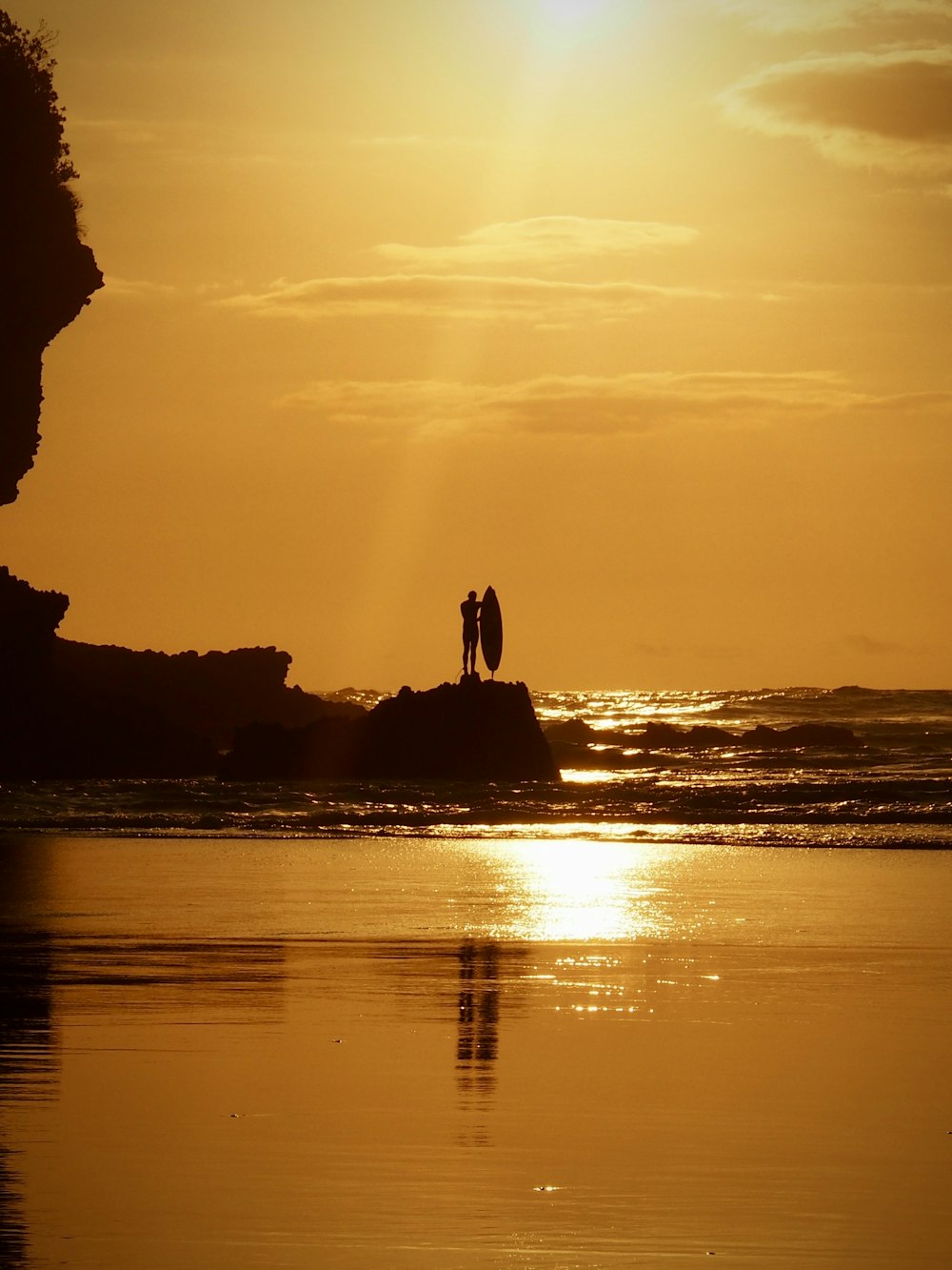 silhouette of man standing on rock formation near body of water during sunset