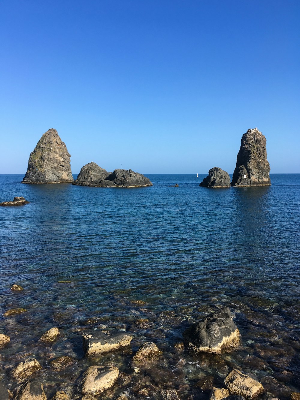 Formación rocosa marrón en el mar azul bajo el cielo azul durante el día