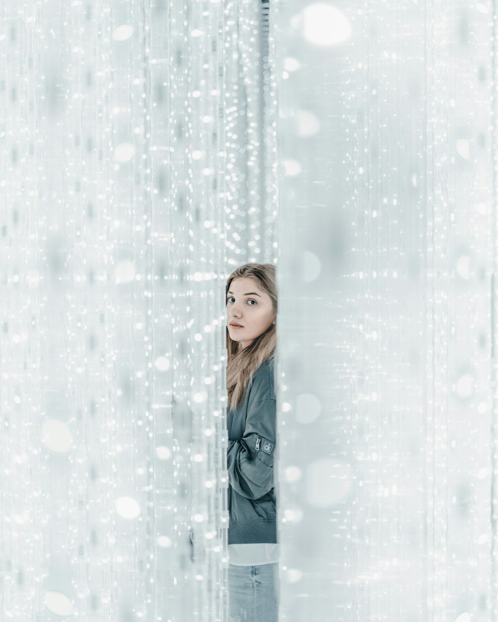 woman in blue and white long sleeve shirt standing beside white curtain