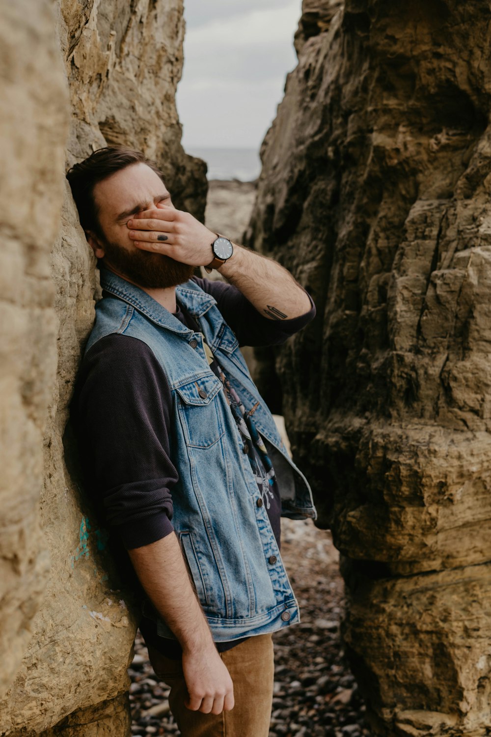 man in blue denim button up shirt and black vest standing beside brown rock formation during