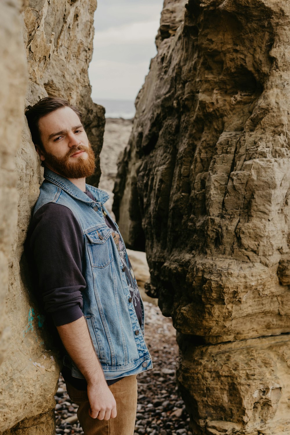 man in black crew neck t-shirt and blue denim jacket standing beside rock formation during