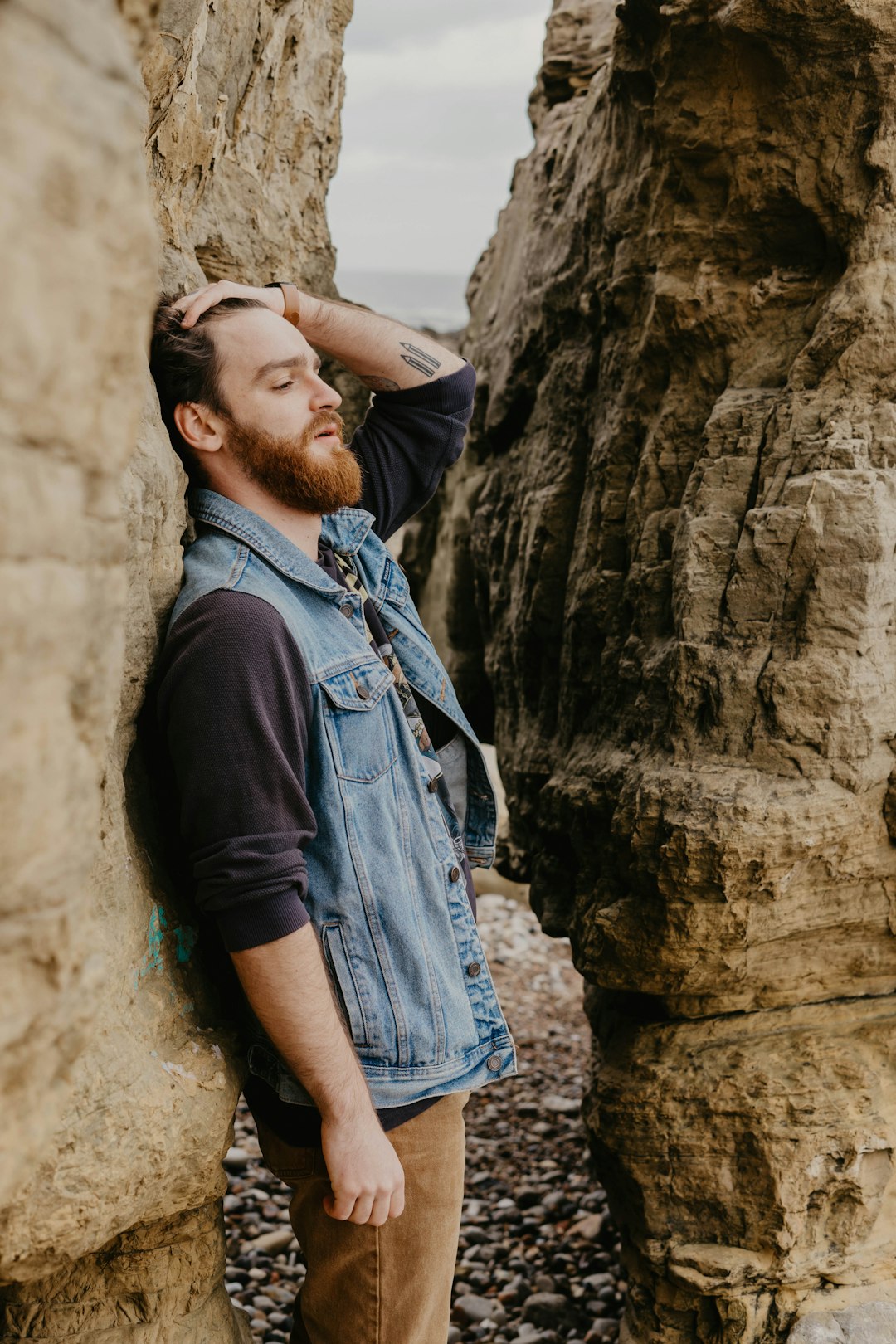 man in black t-shirt and blue denim jeans standing beside brown rock formation during daytime