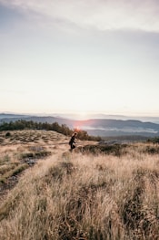 woman in black jacket walking on brown grass field during daytime