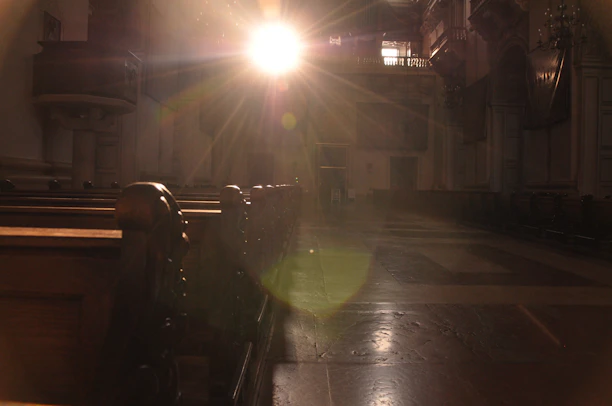 A cozy, sunlit interior of an old church building with wooden pews and stained glass windows.