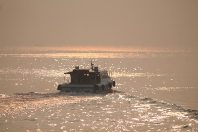 A serene boat gliding gently on calm waters near the Gateway of India at sunset.