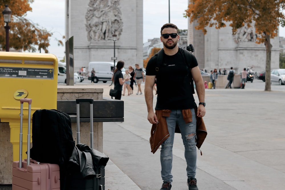 man in black crew neck t-shirt and blue denim jeans standing on sidewalk during daytime